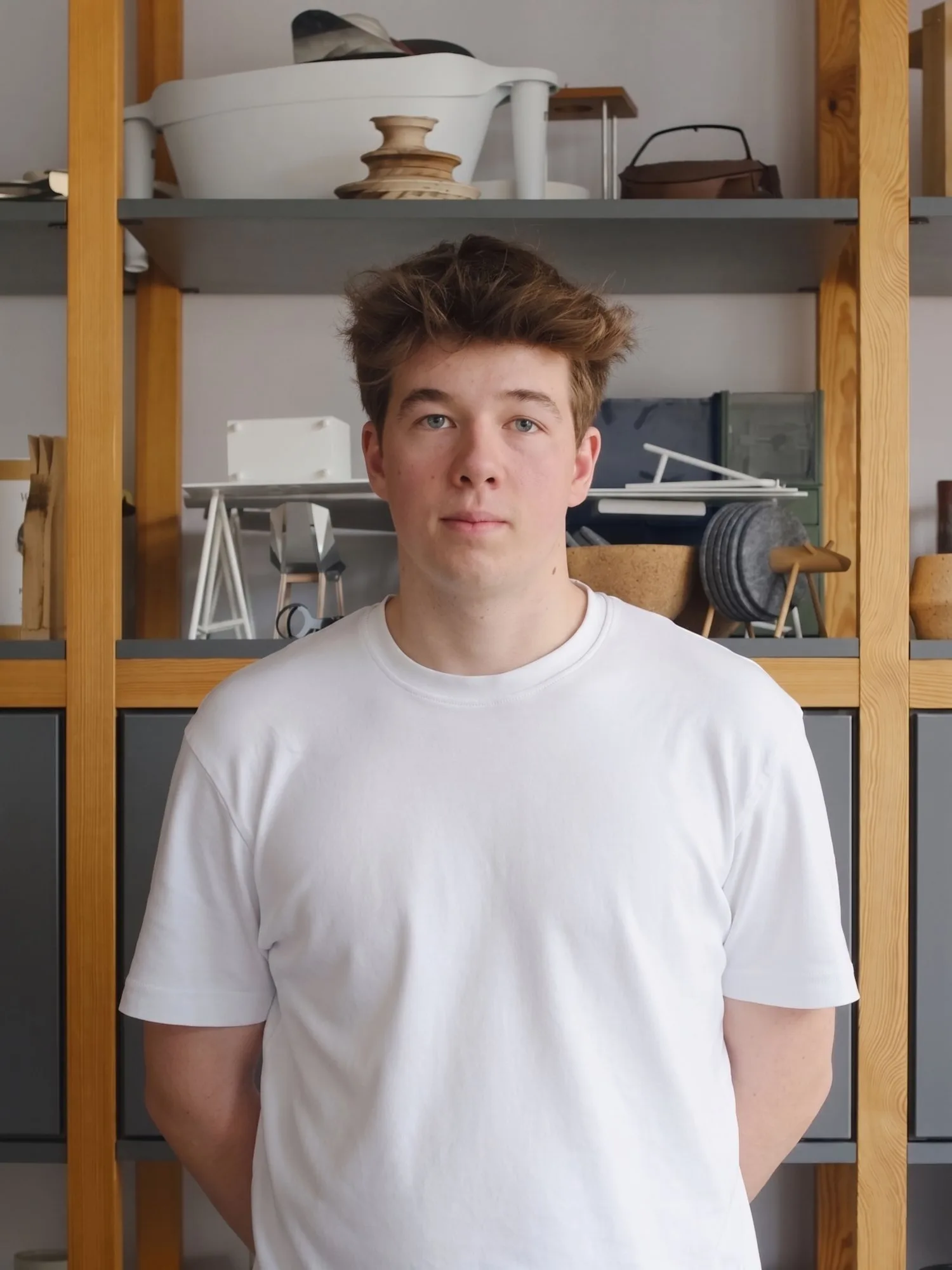 Portrait of Mateusz Pawela in a white T-shirt, standing in front of studio shelves
