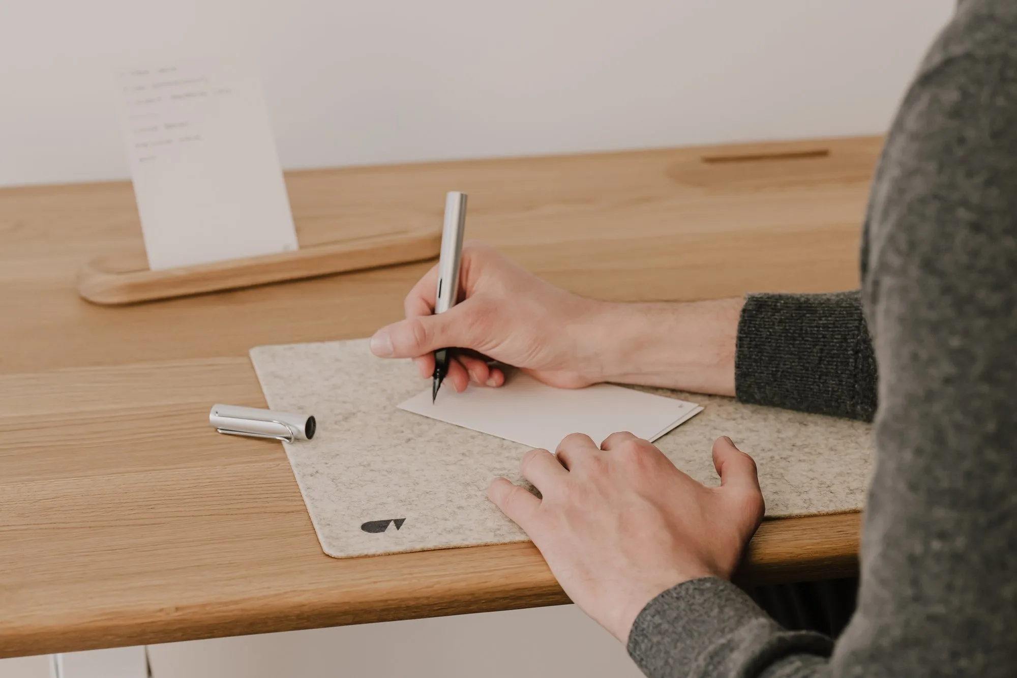 Person writing on a to-do card at an oak desk